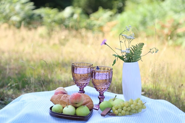 Romantisches, ästhetisches Sommerpicknick mit Croissants, Früchten, Schokoladentrauben und Gläsern Wein im Wald. Cottage-Kernästhetik Sommerstimmung