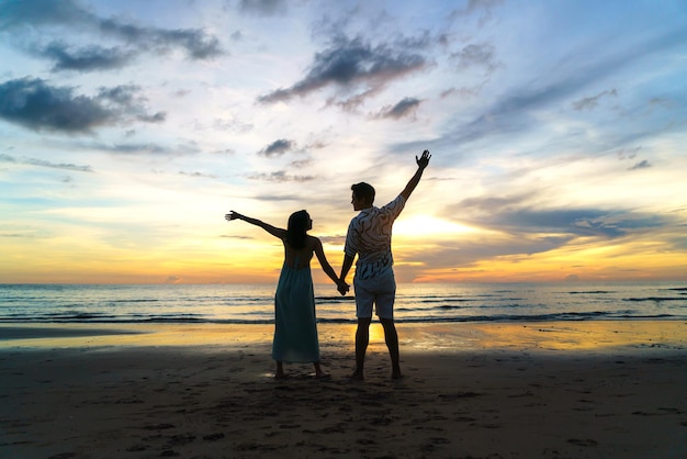 Romantisches asiatisches Paar steht und hält Hand und genießt einen wunderschönen Sonnenuntergang am Strand