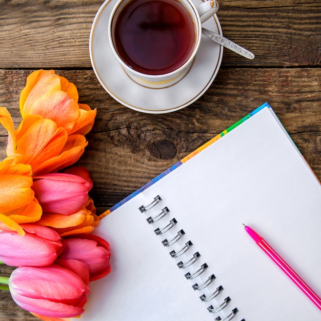 Romantisches Bild mit Tulpen, Tee, Notizbuch auf hölzernem Hintergrund