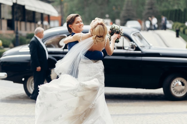 Foto romantisches braut- und bräutigamporträt nach der hochzeitszeremonie glückliches brautpaar, das im freien tanzt luxusauto im hintergrund glücklicher bräutigam, der die braut umarmt