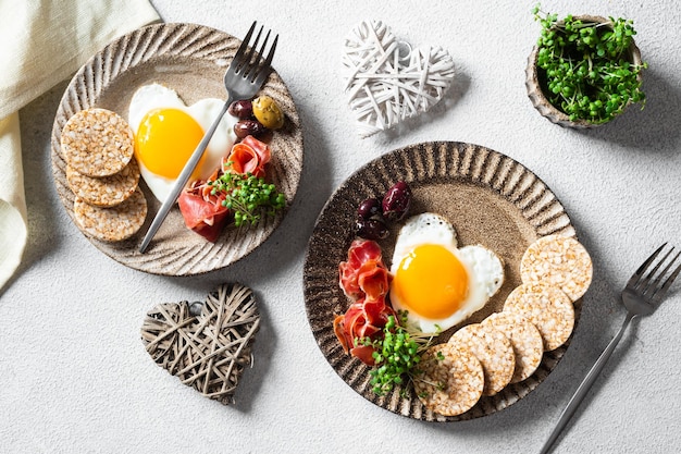 Romantisches Frühstück am Frauentag - Spiegeleier in Form eines Herzens und Oliven. Gesundes Frühstück. Reiskuchen mit Eiern und Hamon. Romantisches Frühstück. Ansicht von oben.