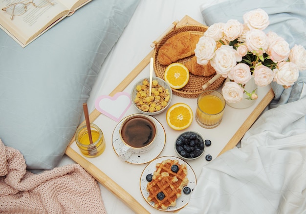 Romantisches Frühstück mit Kaffee, Waffeln, Orangensaft und Rosenblüten.