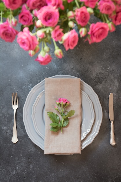 Romantisches Gedeck mit rosa Rosen als Dekor, Weinlesegeschirr, Tafelsilber und Dekorationen.