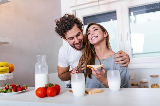 Romantisches junges Paar, das zusammen in der Küche kocht und eine tolle Zeit zusammen hat. Mann und Frau lachen und trinken Milch morgens beim Frühstück