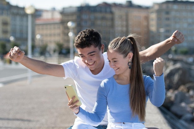 Romantisches multiethnisches Paar, das auf ein Telefon schaut und gute Ergebnisse feiert