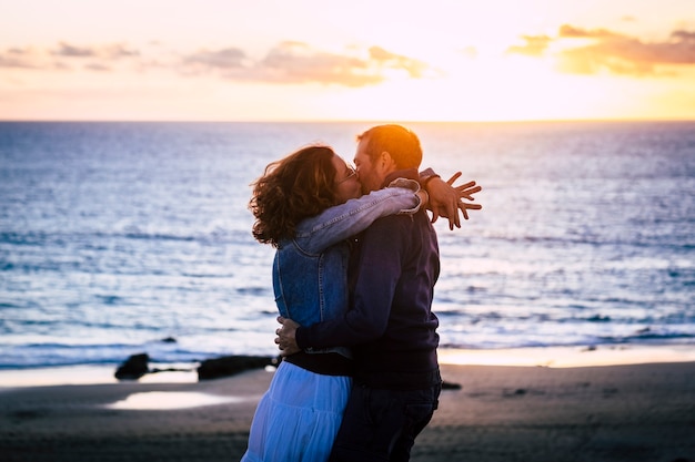 Romantisches Paar, das den Sonnenuntergang am Strand genießt und sich küsst und liebt