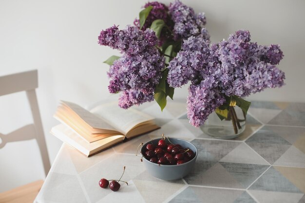 Romantisches Stillleben mit einem offenen Buch, lila Blumen und Kirschen auf einem Tisch