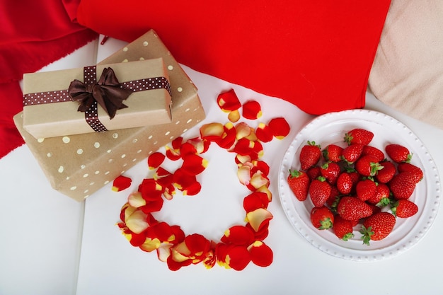 Romantisches Stillleben mit Erdbeergeschenken und Rosenblättern auf dem Sofa