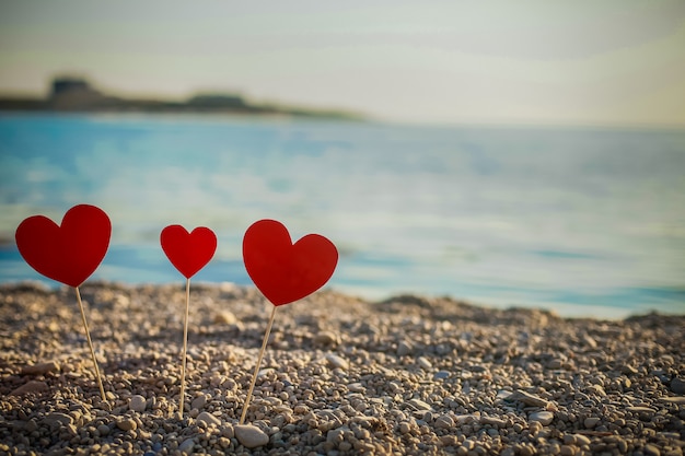 Romantisches Symbol zweier Herzen am Strand. Liebe. Rotes Herz am Sonnenuntergangsmeer. Das Konzept, das ich dich liebe. Valentinstag. Herzen am Strand stehen auf Stöcken