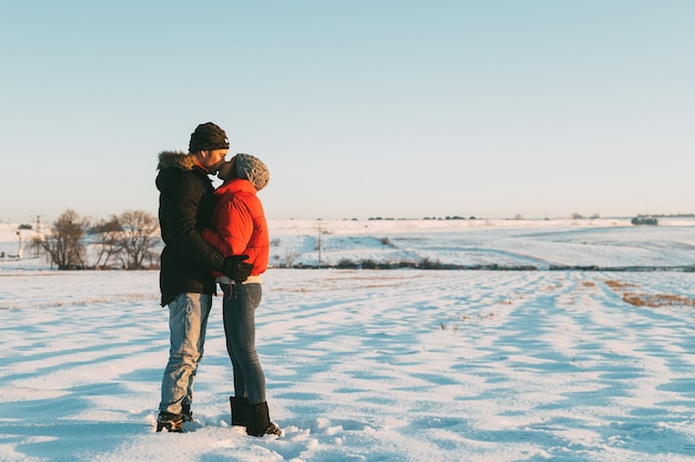 Romantisches verliebtes Paar in warmen Kleidern, die sich sanft in der verschneiten Winterlandschaft umarmen und küssen