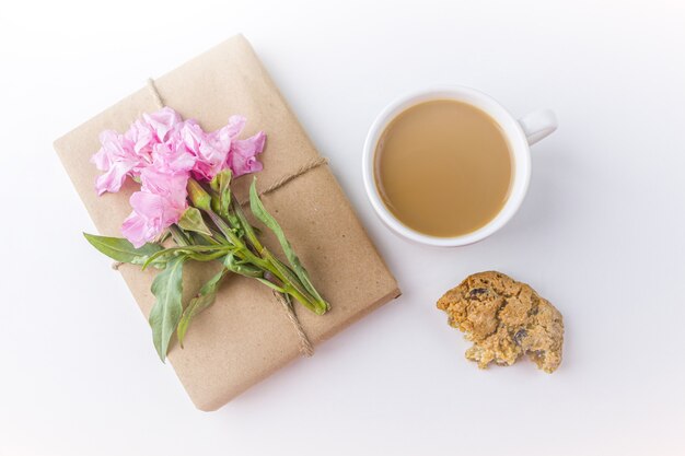 Romantisches Weinlesestillleben mit hübscher Geschenkbox, die mit braunem Bastelpapier eingewickelt und mit rosa Blume auf weißem Hintergrund verziert wird