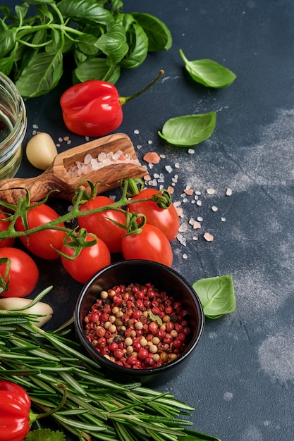 Romero fresco, cilantro, albahaca, tomates cherry, pimientos y aceite de oliva, especias, hierbas y verduras en la mesa de pizarra negra.