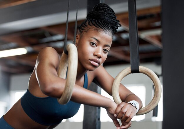 Rompe la gimnasia y el retrato de una mujer negra con anillos para entrenar músculos y brazos en el gimnasio Enfoque fuerte y cara de una gimnasta africana con rendimiento durante un entrenamiento o ejercicio en un club