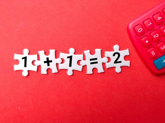 Rompecabezas blanco y calculadora con el número 1 más 1 igual a 2 sobre fondo rojo Concepto de educación