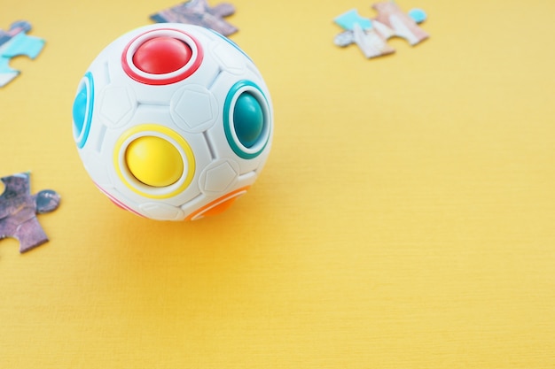 Rompecabezas para niños en forma de una bola con bolas de colores en el interior y detalles de un rompecabezas de cartón sobre un fondo amarillo. Espacio para texto.