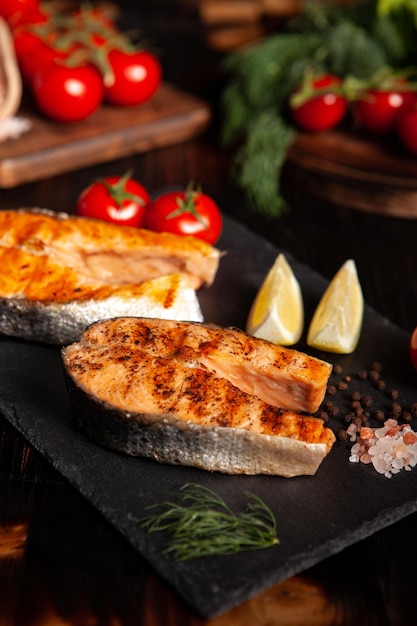 Rondas de salmón cocido colocadas en un plato con unas rodajas de limón al lado. Tomates y ensalada en el fondo