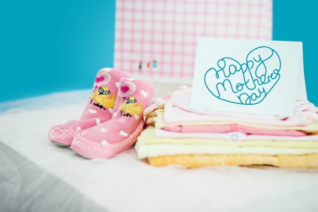 Foto la ropa de bebé con caja de regalo sobre fondo azul. concepto de feliz día de las madres