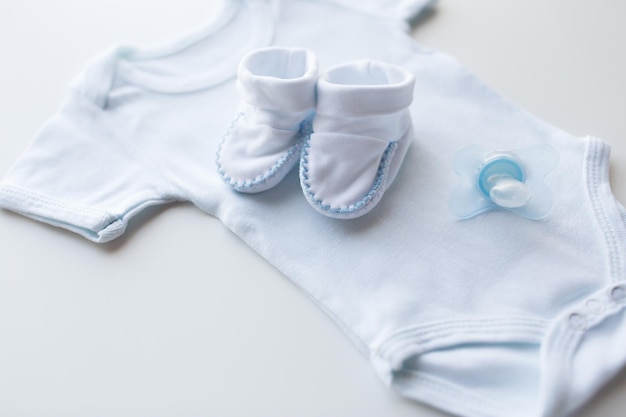 ropa de bebé, infancia, maternidad y concepto de objeto - cierre de mono blanco, patucos y chupete para niño recién nacido en la mesa