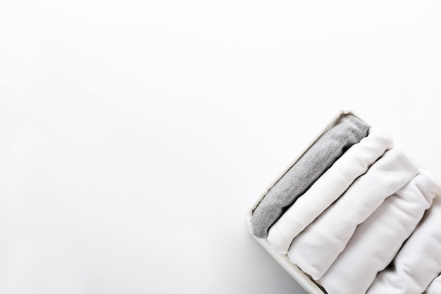Ropa blanca y gris cuidadosamente doblada en un contenedor para un armario o viaje en blanco. Orden en el armario.