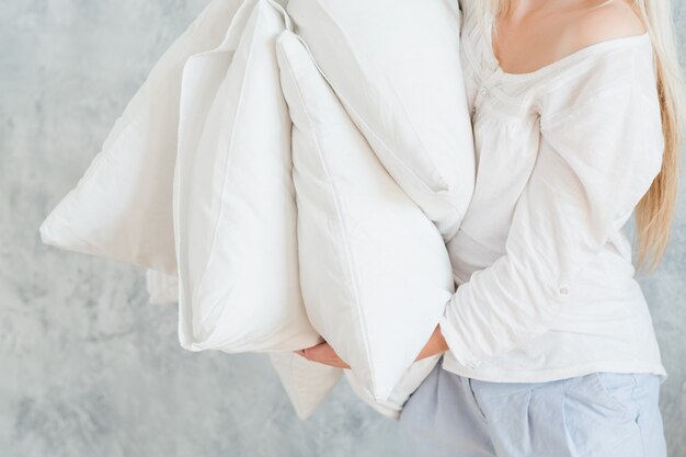 Ropa de cama de calidad. Concepto de sueño profundo. Mujer sosteniendo pila de almohadas.