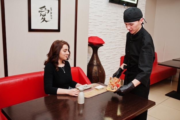 Ropa de chef profesional en negro da sushi y rollos para mujer cliente en un restaurante de comida tradicional japonesa