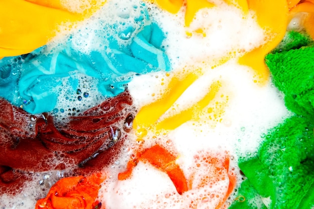 Ropa de color empapada en agua con detergente y burbujas de espuma