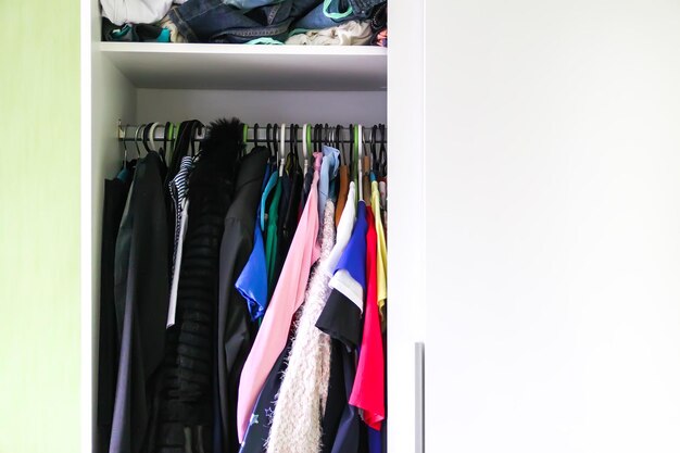 Ropa colorida colgada en perchas en el armario de la casa. Organización de espacios reducidos.