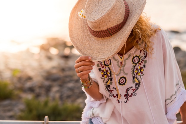 Ropa de estilo de moda y una mujer caucásica irreconocible escondida por un sombrero de vaquero de vacaciones - concepto de viajes y vacaciones de verano con playa desenfocada en un día soleado