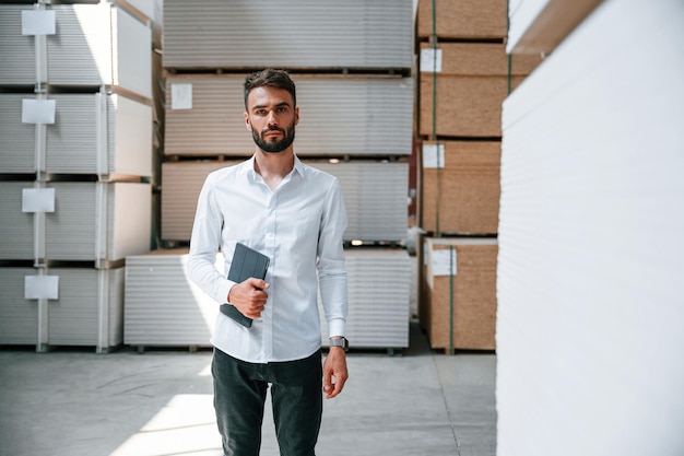 En ropa formal, el trabajador de almacenamiento está en el almacén con un montón de productos.