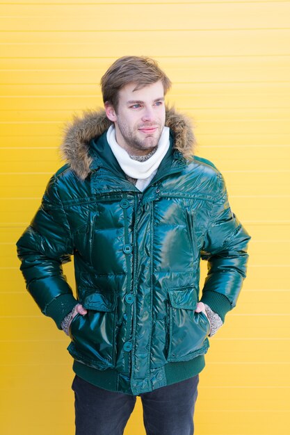 Ropa de hombre con estilo de invierno. El hombre barbudo hipster usa chaqueta abrigada con fondo amarillo de piel. Guy usa chaqueta abrigada con capucha. Siéntete cómodo con ropa abrigada. Manténgase caliente. Ropa de invierno cómoda.