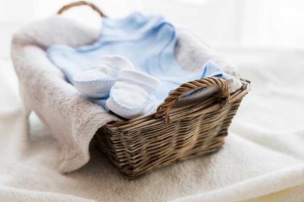 ropa, infancia, maternidad y concepto de objeto - cierre de patucos de bebé blancos con un montón de ropa y toalla para un niño recién nacido en una cesta sobre la mesa