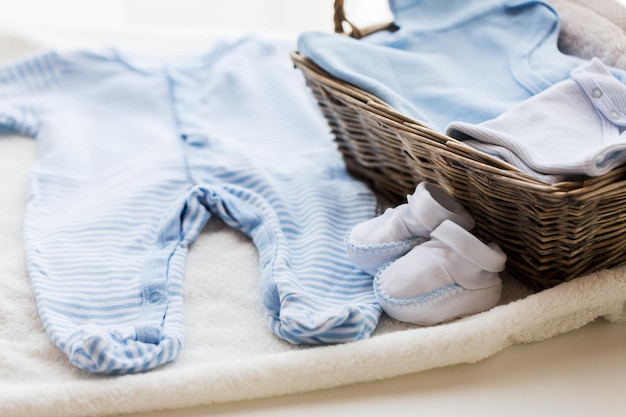 ropa, infancia, maternidad y concepto de objeto - cierre de patucos de bebé blancos con un montón de ropa y toalla para un niño recién nacido en una cesta sobre la mesa