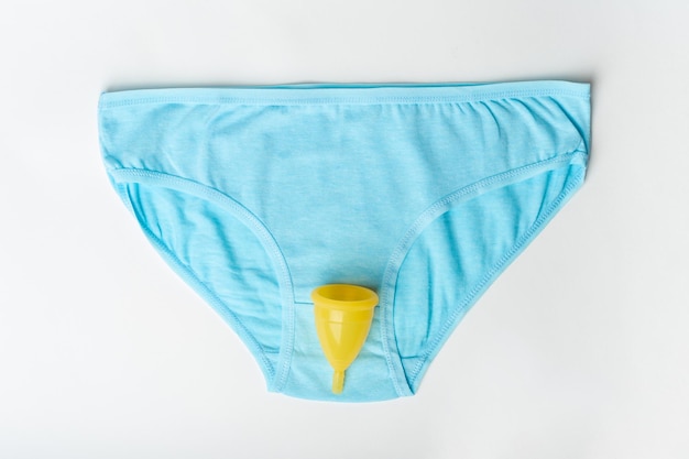 Ropa interior azul femenina y copa menstrual amarilla sobre fondo blanco Concepto de salud de la mujer