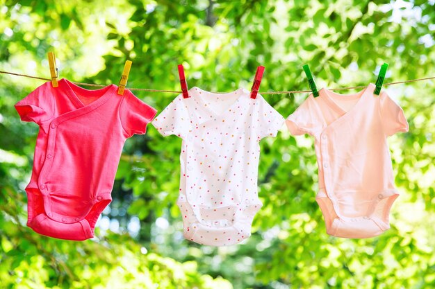 Ropa linda de bebé colgada en el tendedero al aire libre. Lavandería infantil colgada en línea en el jardín sobre fondo verde. Accesorios para bebés.