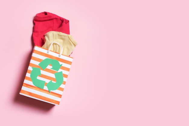Ropa para niños en una bolsa de compras con un símbolo de reciclaje Concepto de reciclaje de ropa de donación de segunda mano