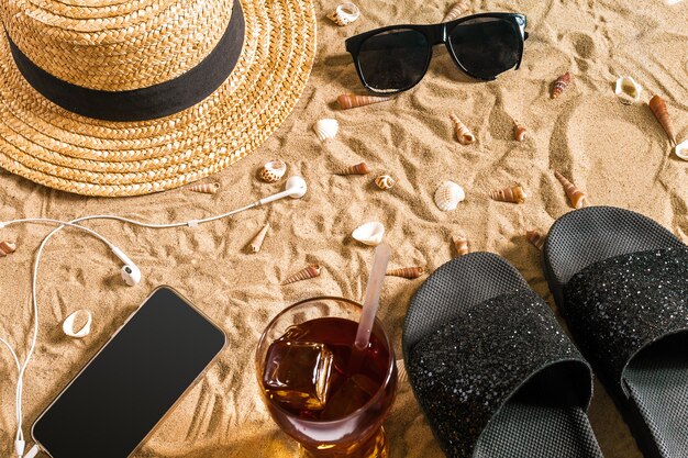 Ropa de playa de verano, chanclas, gorro, gafas de sol y conchas marinas en la playa de arena