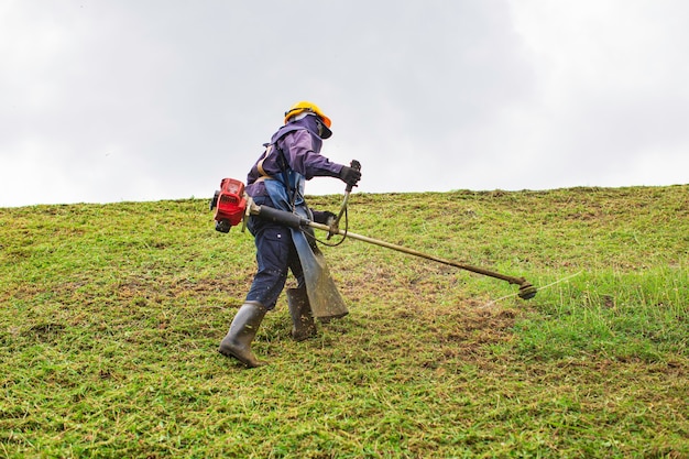 Ropa de trabajo femenina ropa protectora corta en la colina el césped con una cortadora de césped