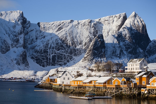 Rorbu de casa de madera tradicional noruego para pararse en la orilla del fiordo y las montañas en la distancia. Islas Lofoten. Noruega.