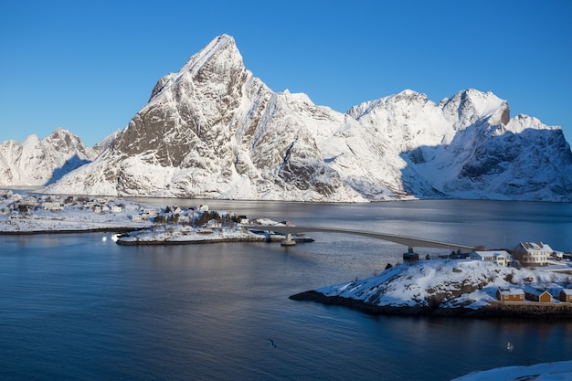 Rorbu de casa de madera tradicional noruego para pararse en la orilla del fiordo y las montañas en la distancia. Islas Lofoten. Noruega.