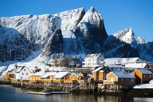 Rorbu de casa de madera tradicional noruego para pararse en la orilla del fiordo y las montañas en la distancia. Islas Lofoten. Noruega.