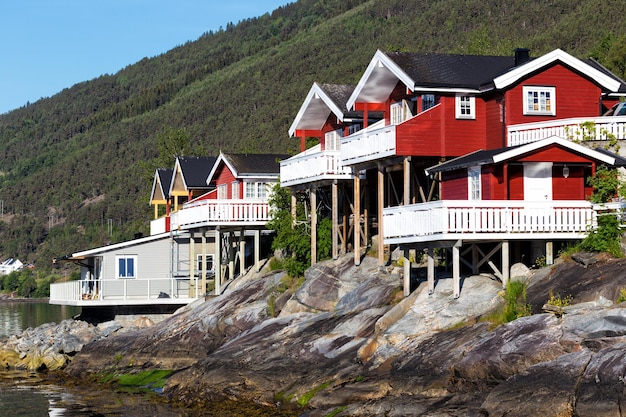 Rorbuer - casa de madera roja tradicional noruega para pararse en la orilla del lago y las montañas en la distancia, noruega