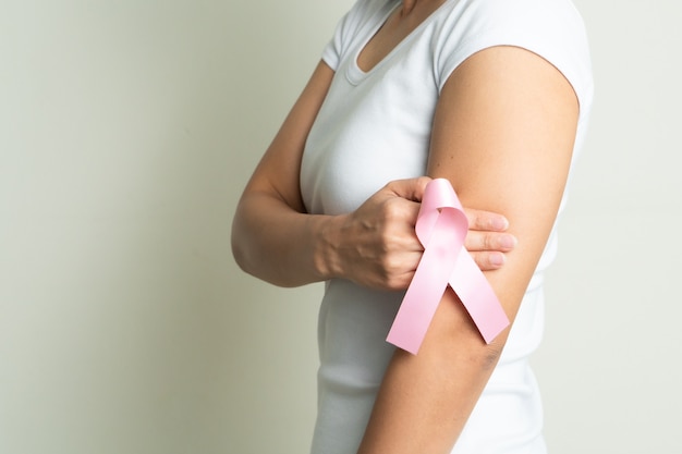 Rosa Abzeichenband auf Frauenhand, die Brust berührt, um Brustkrebsursache zu unterstützen. Konzept zur Aufklärung über Brustkrebs
