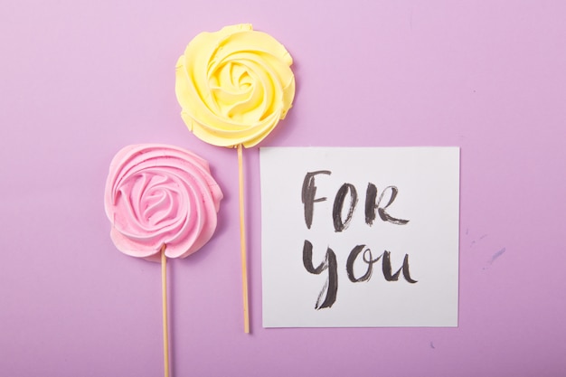 Rosa amarilla y rosa caramelo en colores pastel en un palo de madera con la tarjeta "para ti" sobre un fondo de color, San Valentín, Día de la Madre.