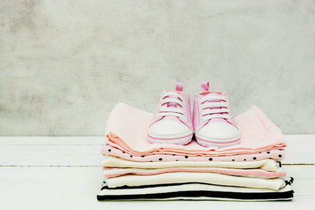 Rosa Babyschuhe und neugeborene Kleidung. Mutterschafts-, Bildungs- oder Schwangerschaftskonzept mit Kopierraum.