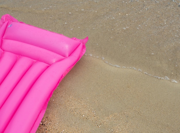 Rosa Bettmatratze schwimmen auf dem Sand am Strand Mit Platz für Ihren Text