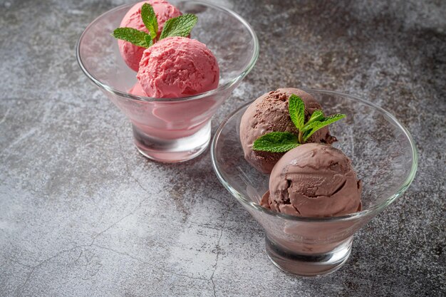 Rosa bolas de helado de fresa y chocolate en una taza contra una mesa de piedra gris