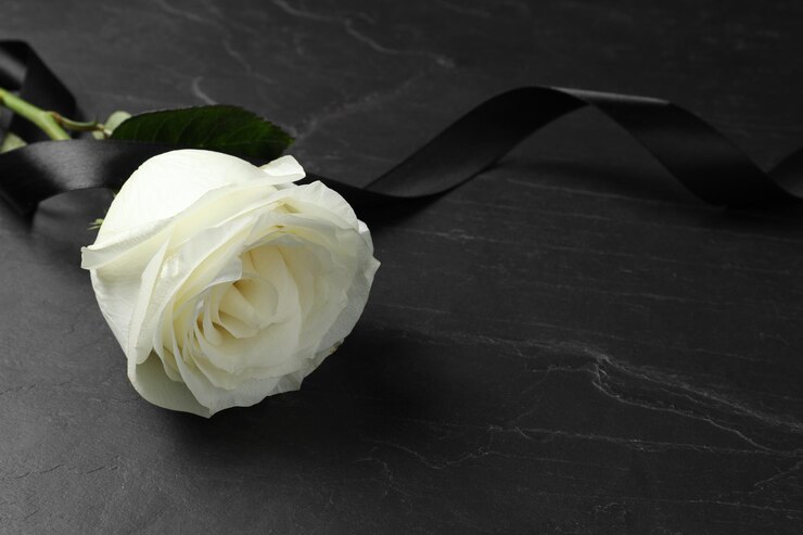 Foto rosa branca e fita em mesa preta em close-up com espaço para texto símbolos funerários