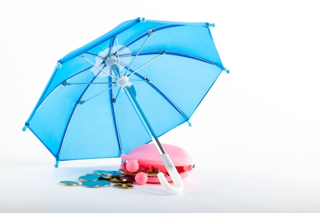 Rosa Brieftasche mit Münzen unter einem blauen Regenschirm auf weißem Hintergrund Versicherungskonzept