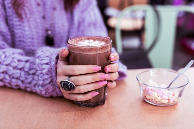 Foto uñas rosa claro. mujer en suéter violeta grueso bebiendo cacao recién hecho mientras está sentado en la mesa