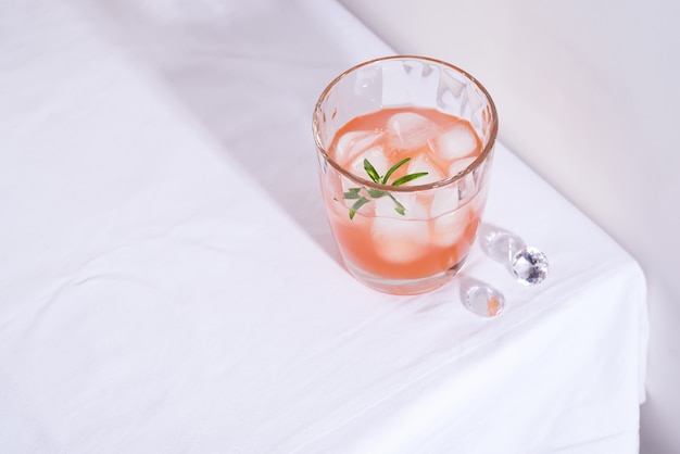 Rosa Cocktail mit Rosmarin und Eis im Glas auf einer weißen Tischdecke auf dem Tisch